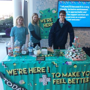Three students standing behind a branded table.