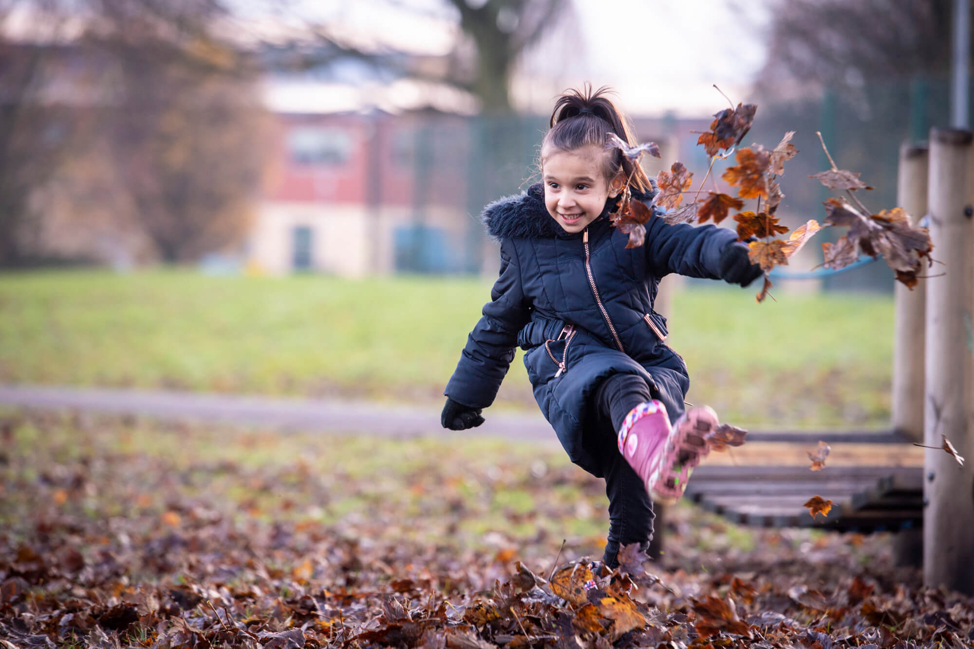 Photograph of a child in wellies kicking leaves