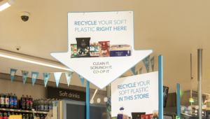 Large point of sale arrow hanging from co op store ceiling with words recycle your soft plastic right here and image of crisps, cereal and bread. Caption says Clean it scrunch it co-opit.