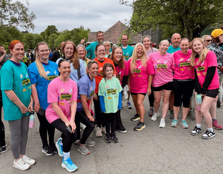 A large group of smiling runners wearing 'Join the Fostering Family' t-shirts at local park run, as part of the fostering recruitment campaign.