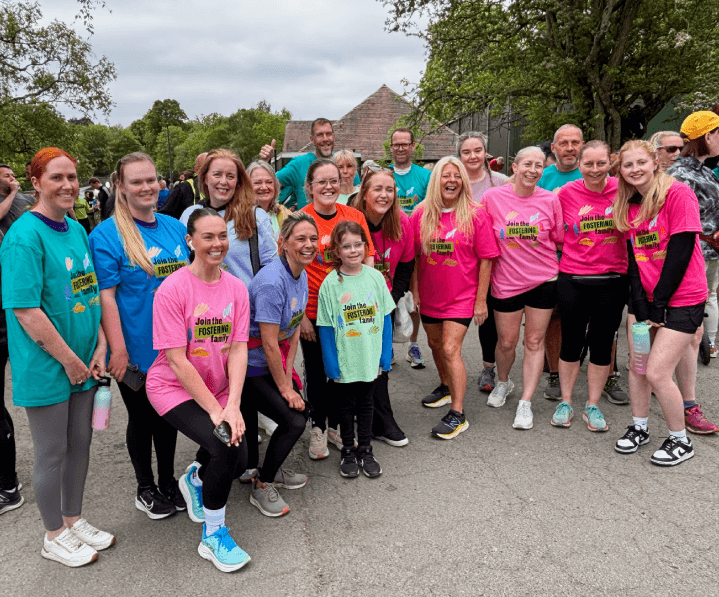 A large group of smiling runners wearing 'Join the Fostering Family' t-shirts at local park run, as part of the fostering recruitment campaign.